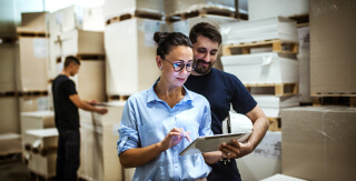 A woman and a man looking at a tablet in a warehouse.